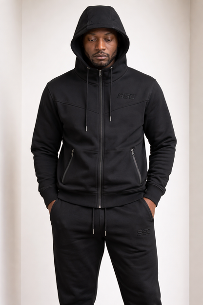Black SSC CORE Black Tech Suit, model wearing matching full-zip hoodie and joggers with hood up.